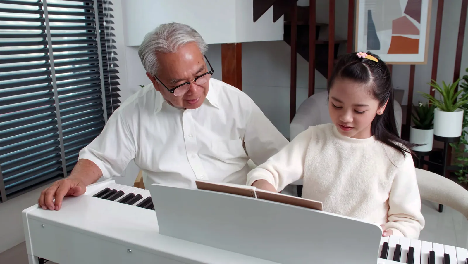 A grandfather teaching his granddaughter to play piano